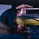 Ein Mann kniet neben einer Frau am Boden, die dramatisch daliegt. Im Hintergrund ist eine weitere Figur auf einem Sofa zu sehen.