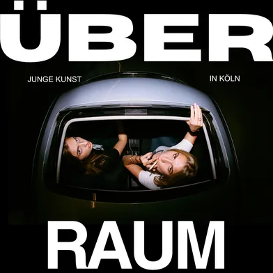 Zwei junge Frauen blicken durch das offene Schiebedach eines Autos nach oben. Umrahmt wird das Bild von großem, weißem Text: „ÜBER RAUM – Junge Kunst in Köln“. Die Szene wirkt urban, provokant und künstlerisch inszeniert.