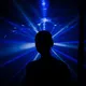 Eine Person steht als schwarze Silhouette vor intensiv blauem Licht. Strahlen breiten sich fächerförmig hinter dem Kopf aus. Geschlecht und Hautfarbe sind wegen der vollständigen Silhouette nicht erkennbar. Die Szene wirkt dunkel und mystisch.